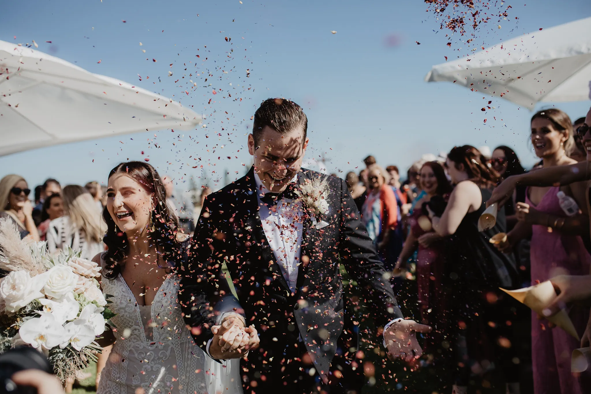 Bride and groom laughing as guests throw confetti