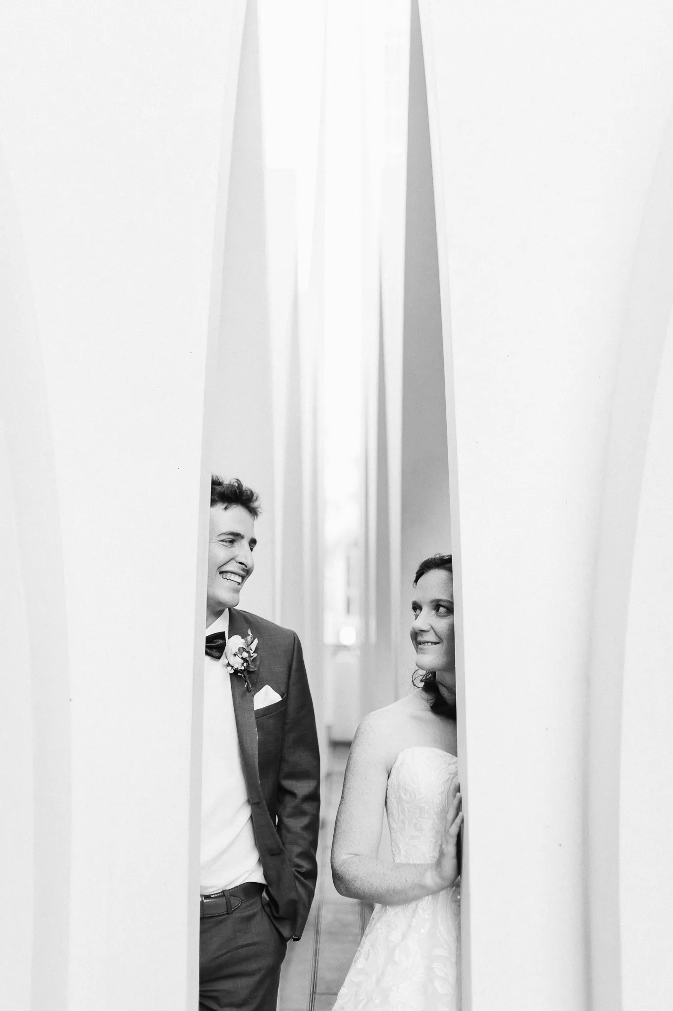 Groom and bride glancing at each other between tall white panels