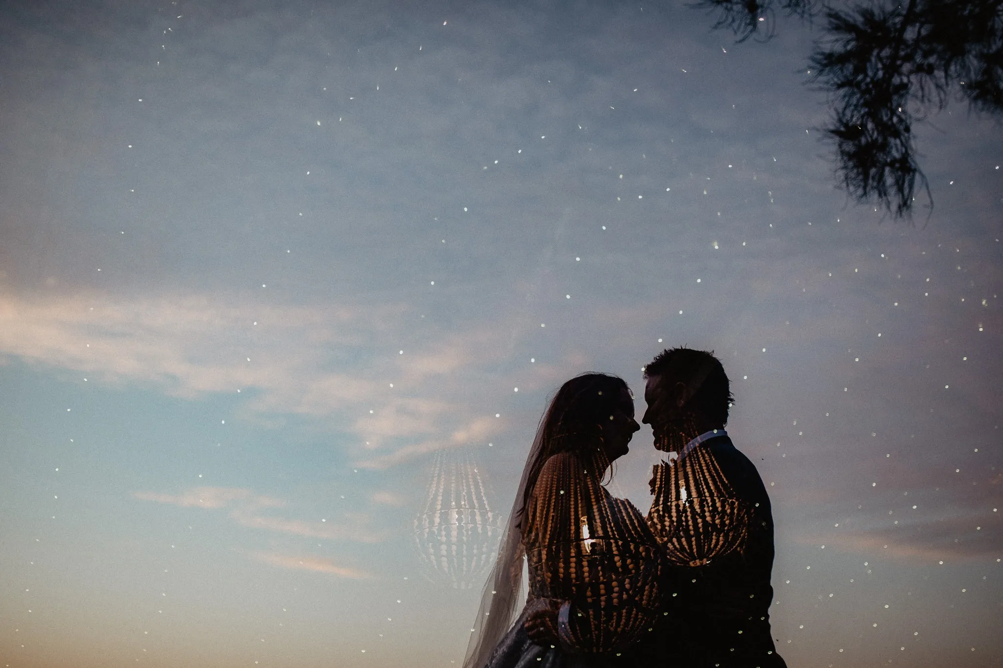 Silhouetted couple against a dusk sky with a chandelier reflection