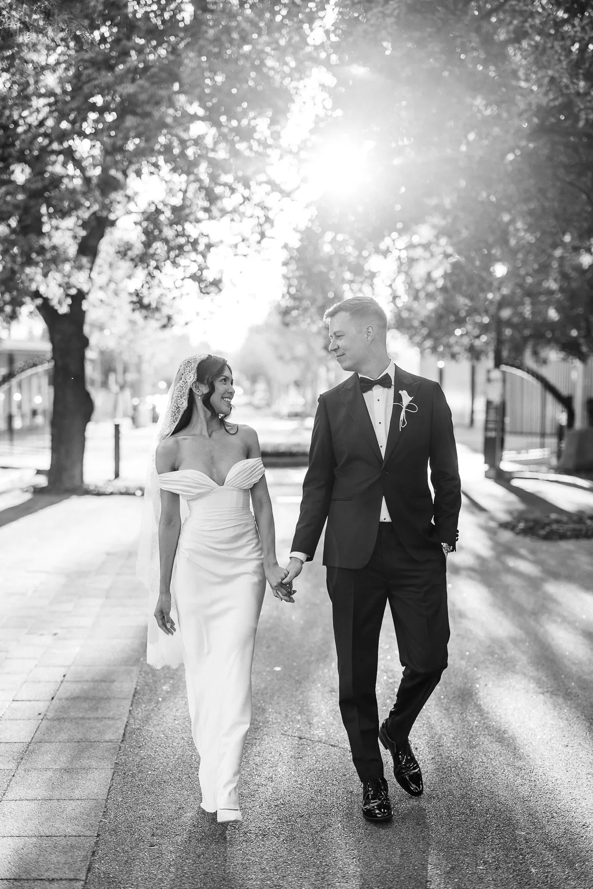 Black and white photo of a bride and groom walking hand in hand