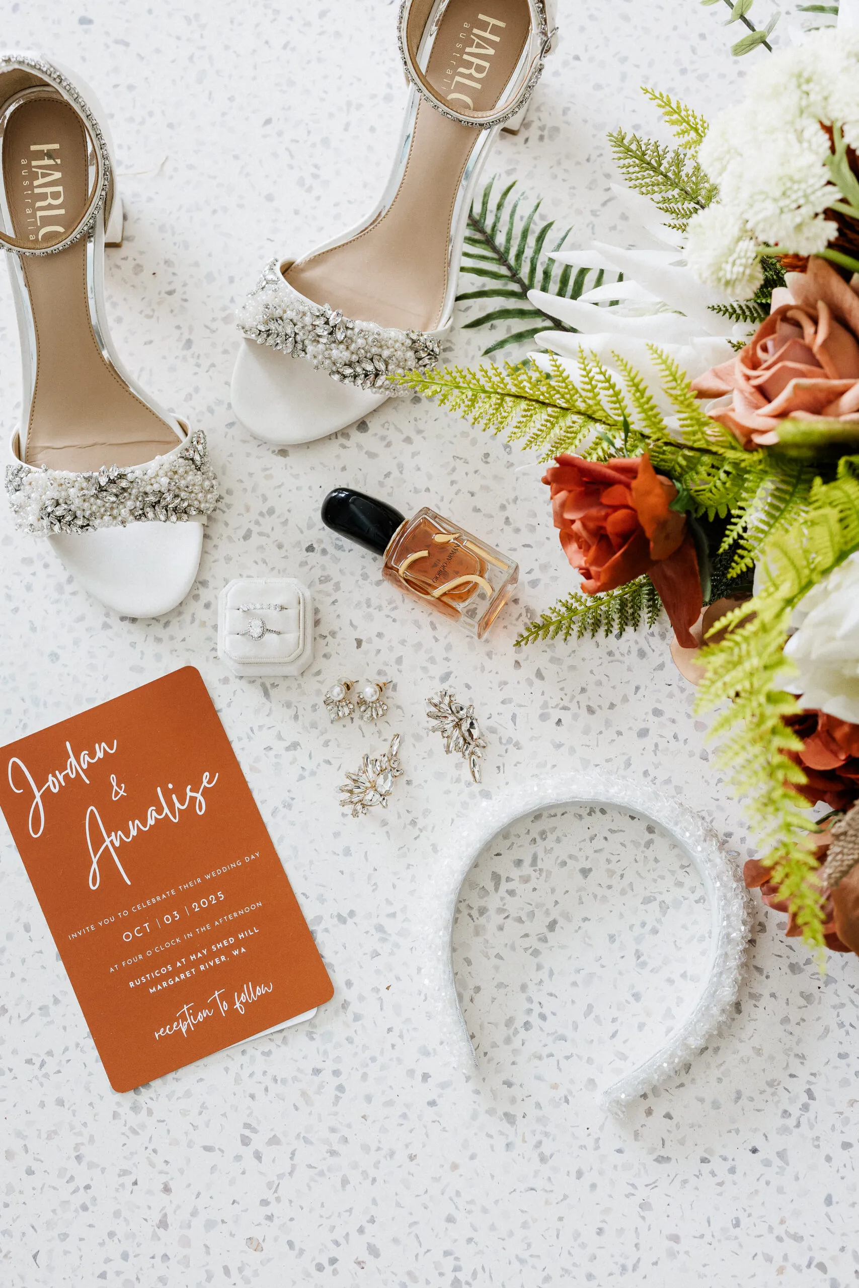 Wedding shoes, invitation, perfume and flowers laid out flat