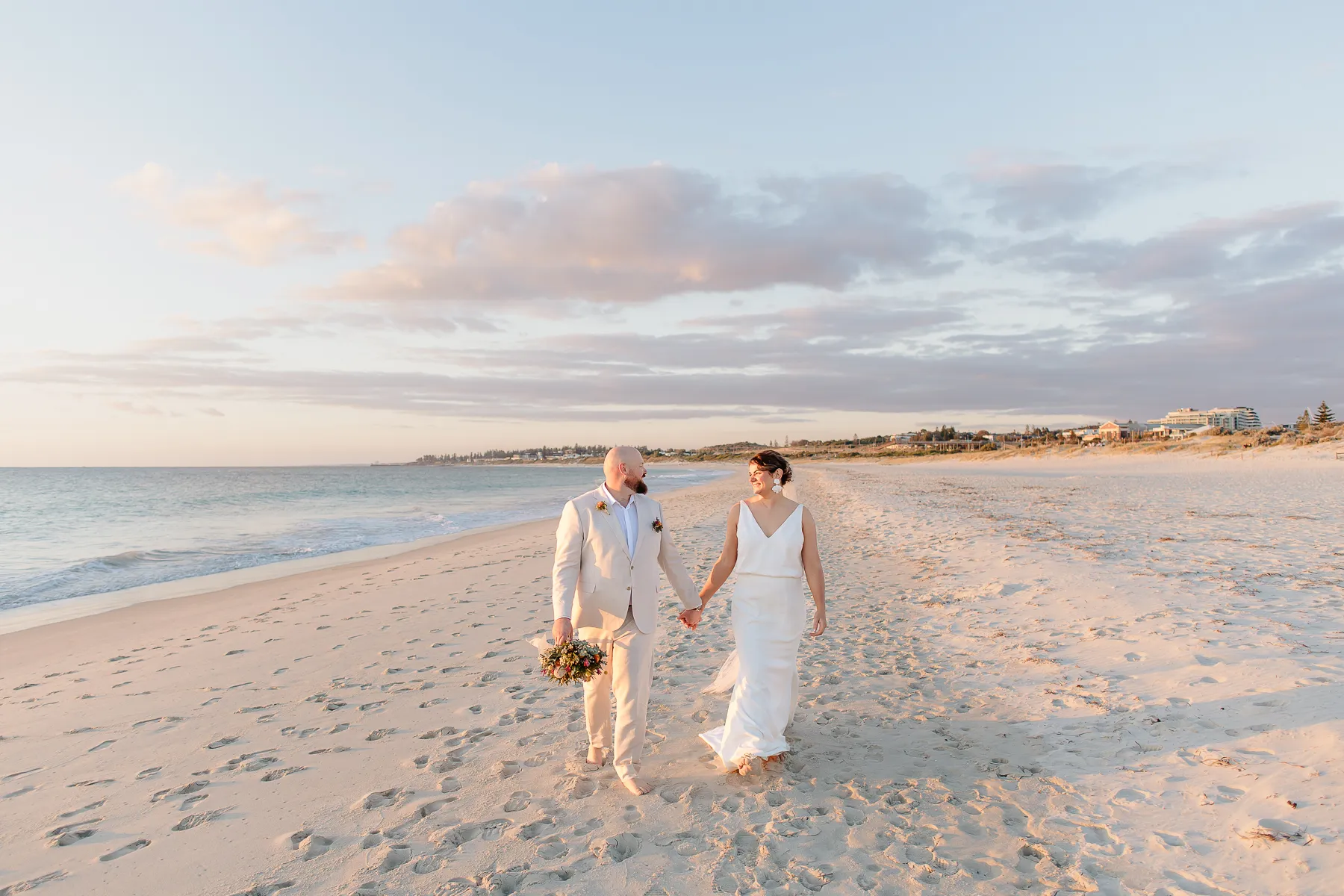 Newlyweds walking hand in hand along the beach at sunset