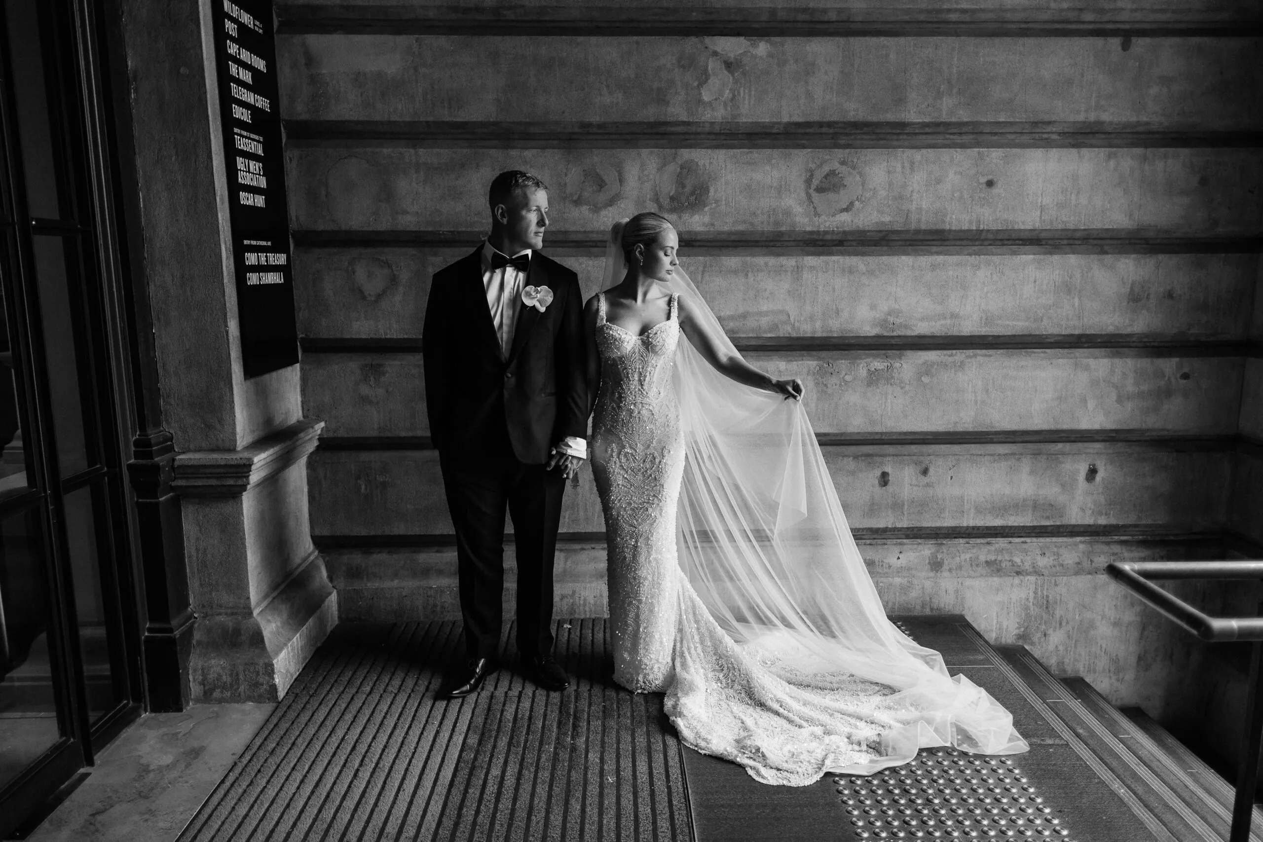 Bride holding her veil beside the groom in a stone doorway, black and white