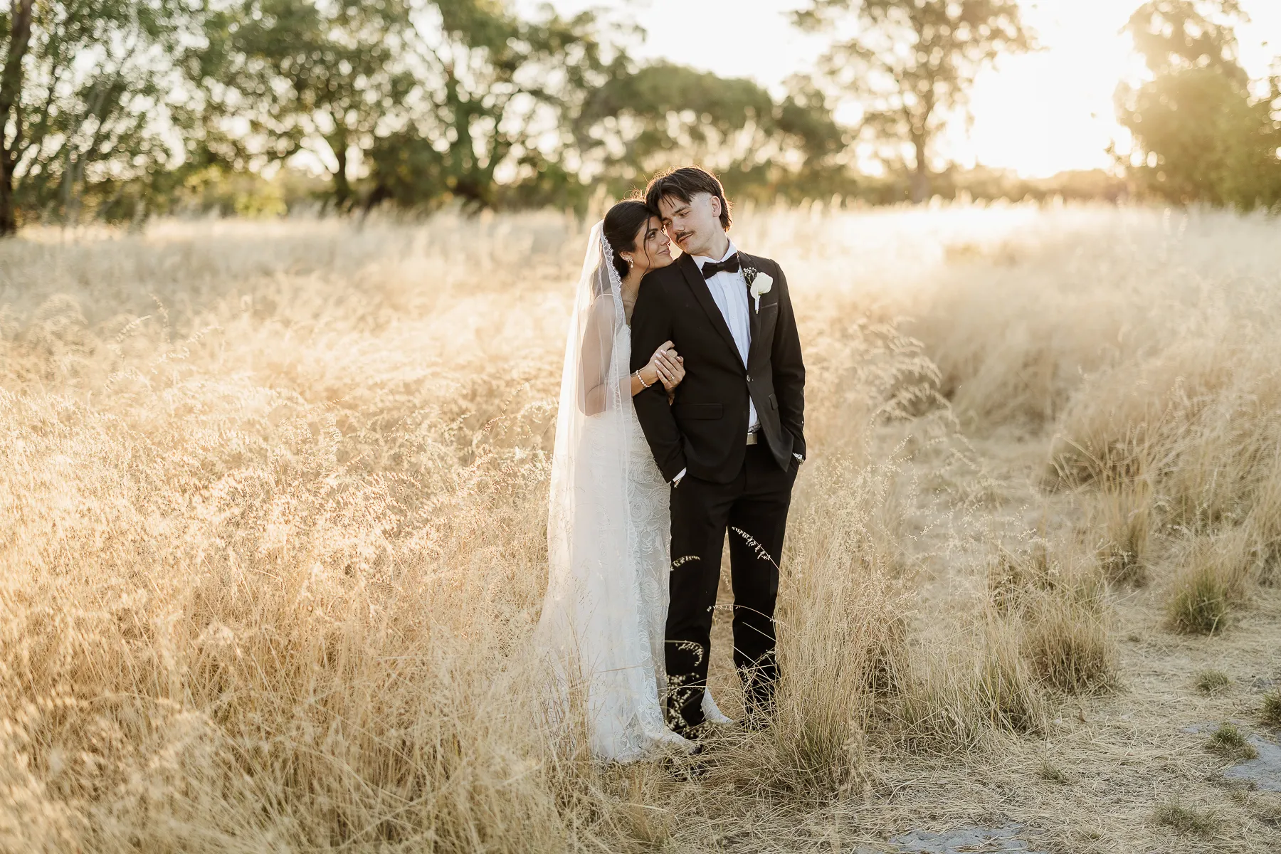 Couple embracing in golden long grass at sunset