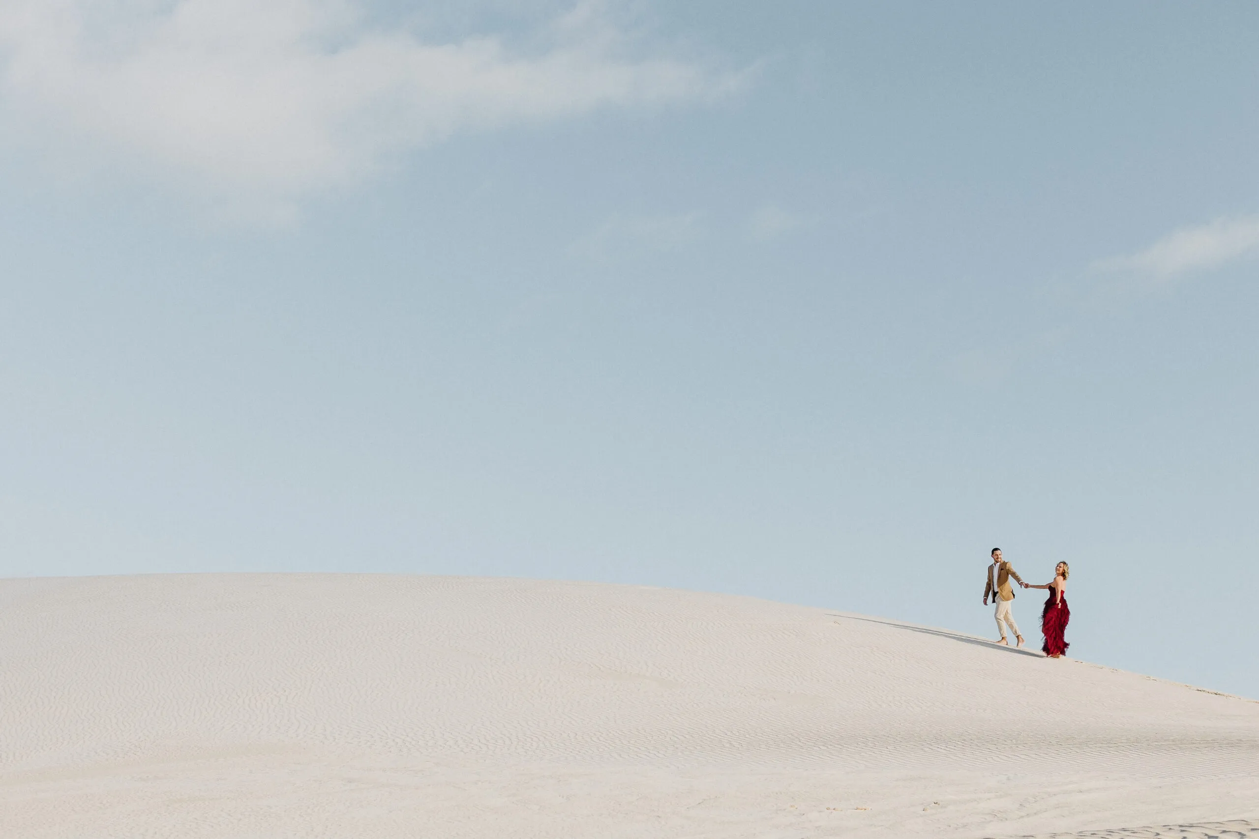 Couple small on a white sand dune under a wide sky