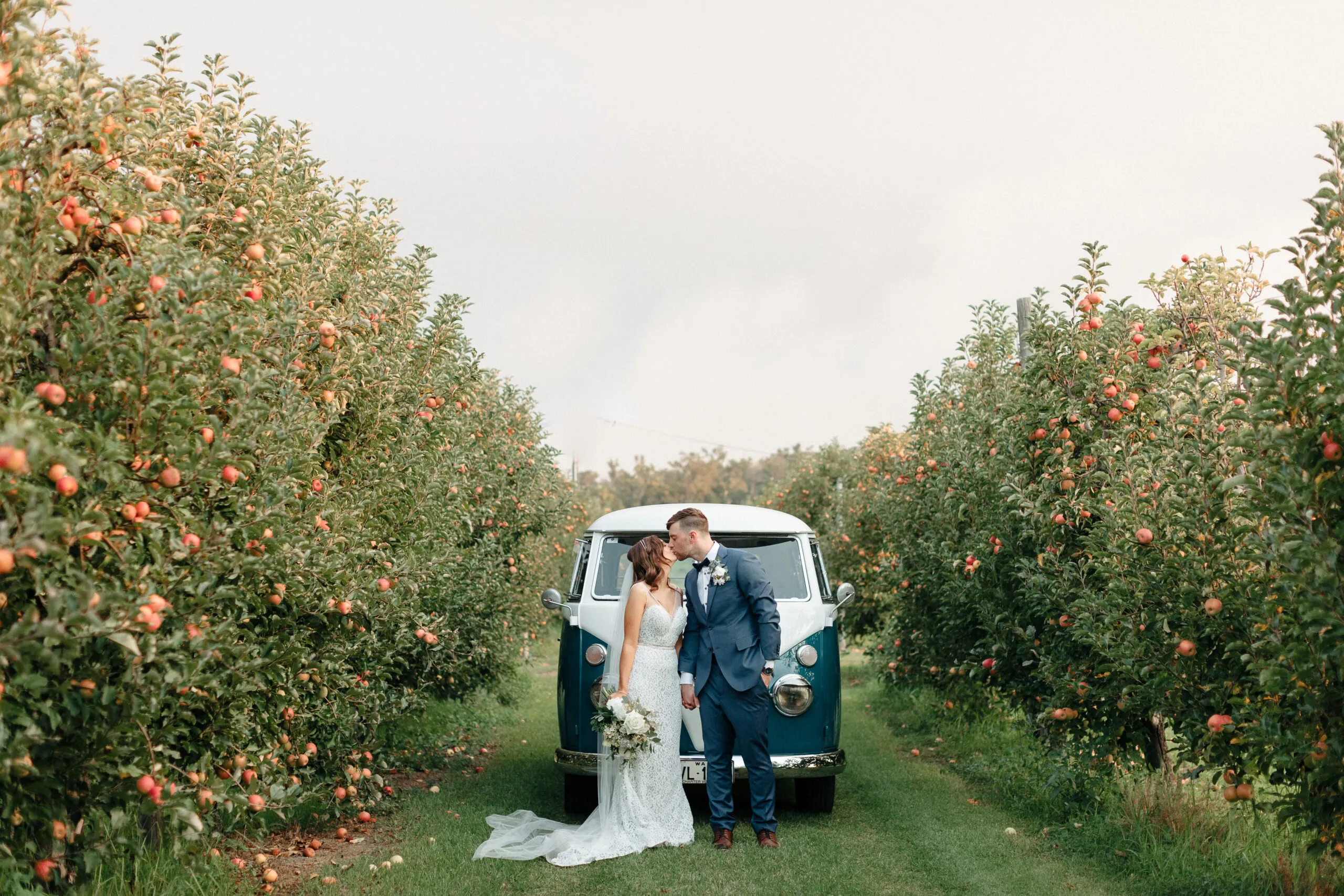 Couple kissing beside a vintage van in an apple orchard